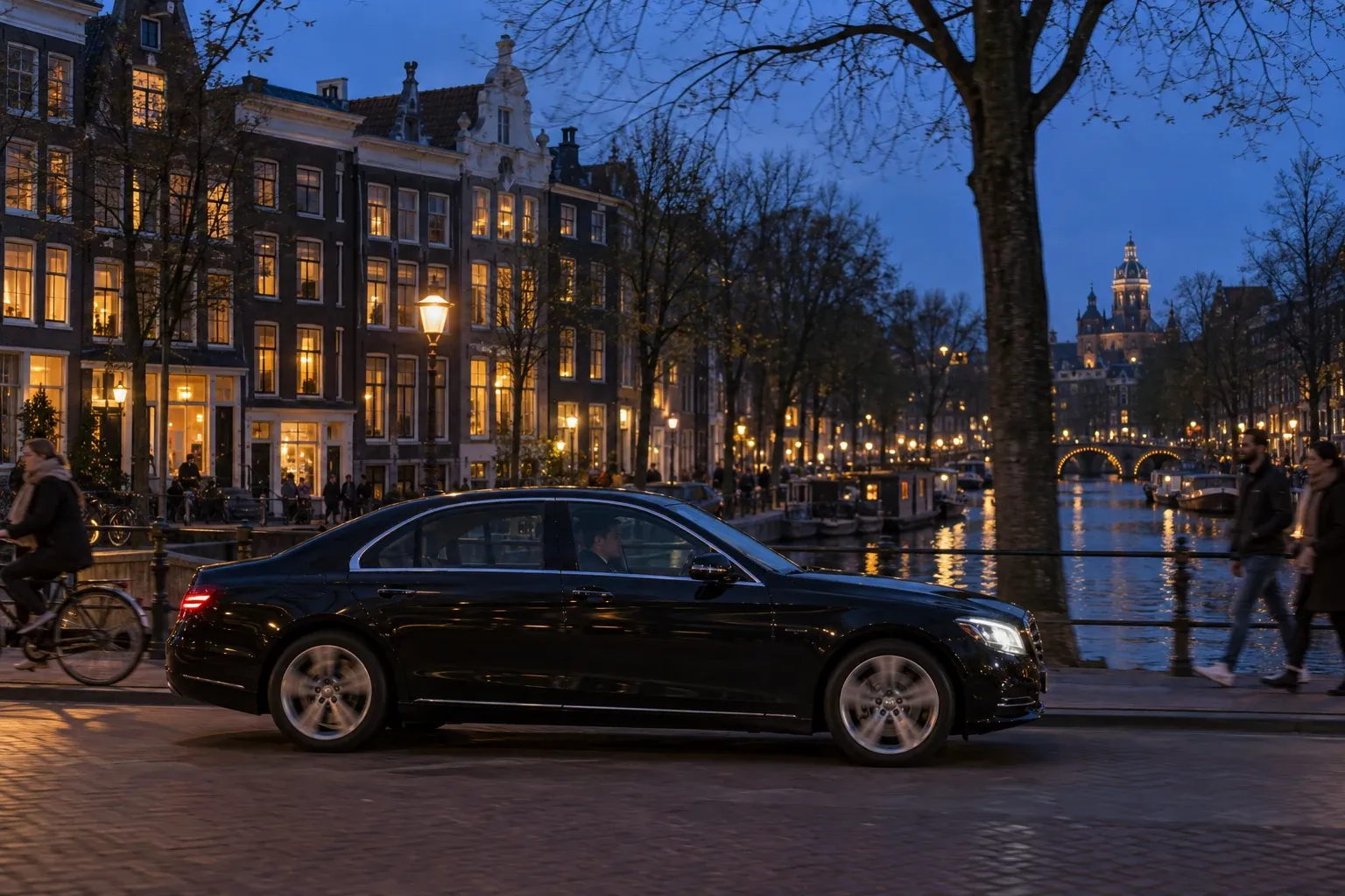 Een zwarte auto rijdt in het blauwe uur langs een gracht, achter de warm verlichte ramen van grachtenpanden.